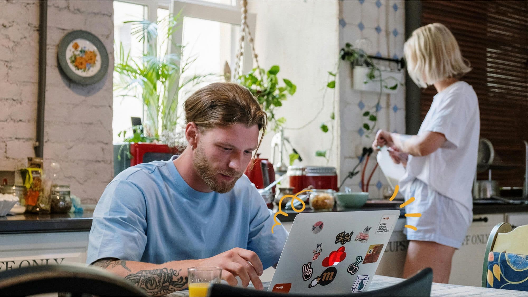 Man working on a laptop and a woman in the kitchen